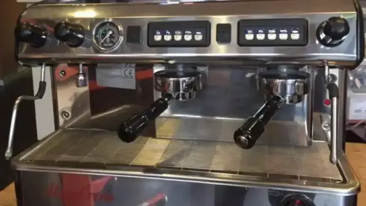 A commercial espresso machine with two brewing groups, steam wands and a pressure gauge.