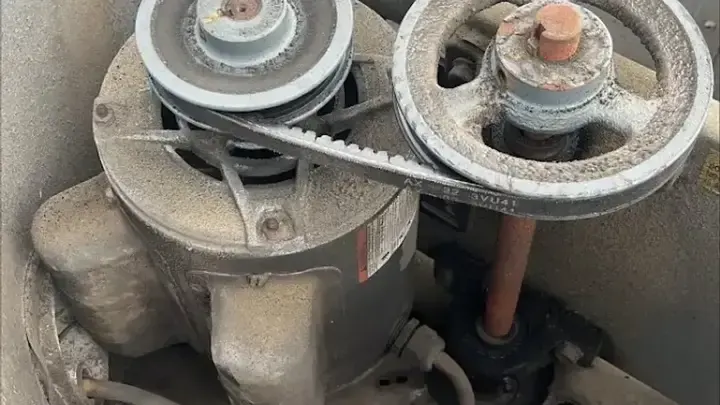 A close view of a motor, belt and pulleys inside an equipment housing.