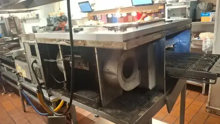 Removed panels expose the oven blower area, wiring and drive components beside the conveyor.